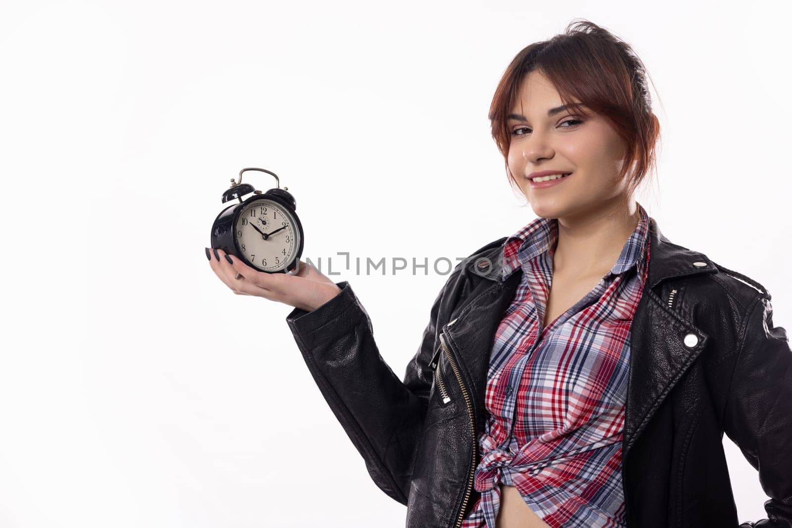 A trendy young woman confidently poses with an alarm clock, showcasing her stylish outfit and vibrant demeanor