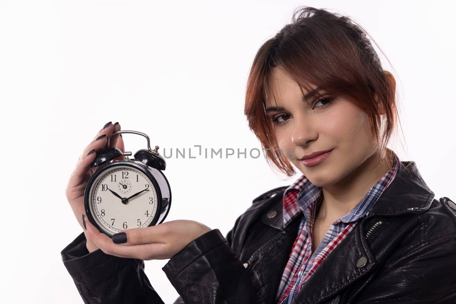 A stylish and fashionable young woman strikes a pose with a vintage alarm clock set against a plain white background