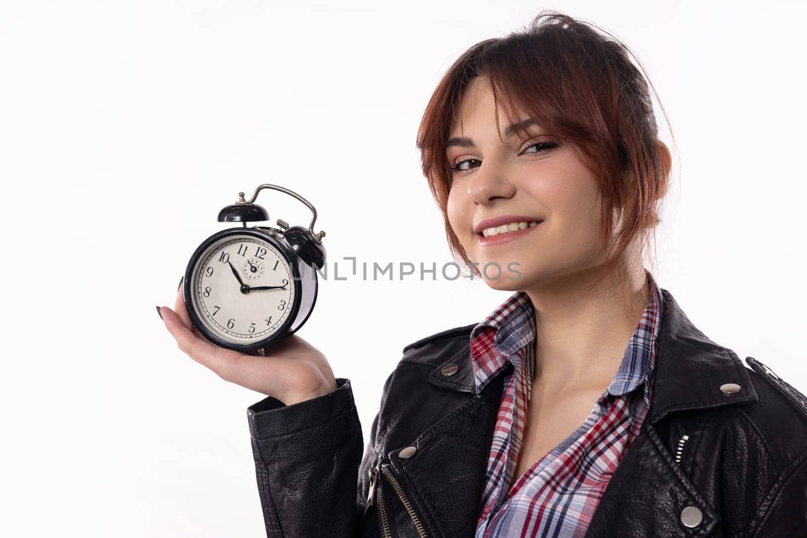 A cheerful young woman confidently poses with an alarm clock, showcasing her style and time management skills