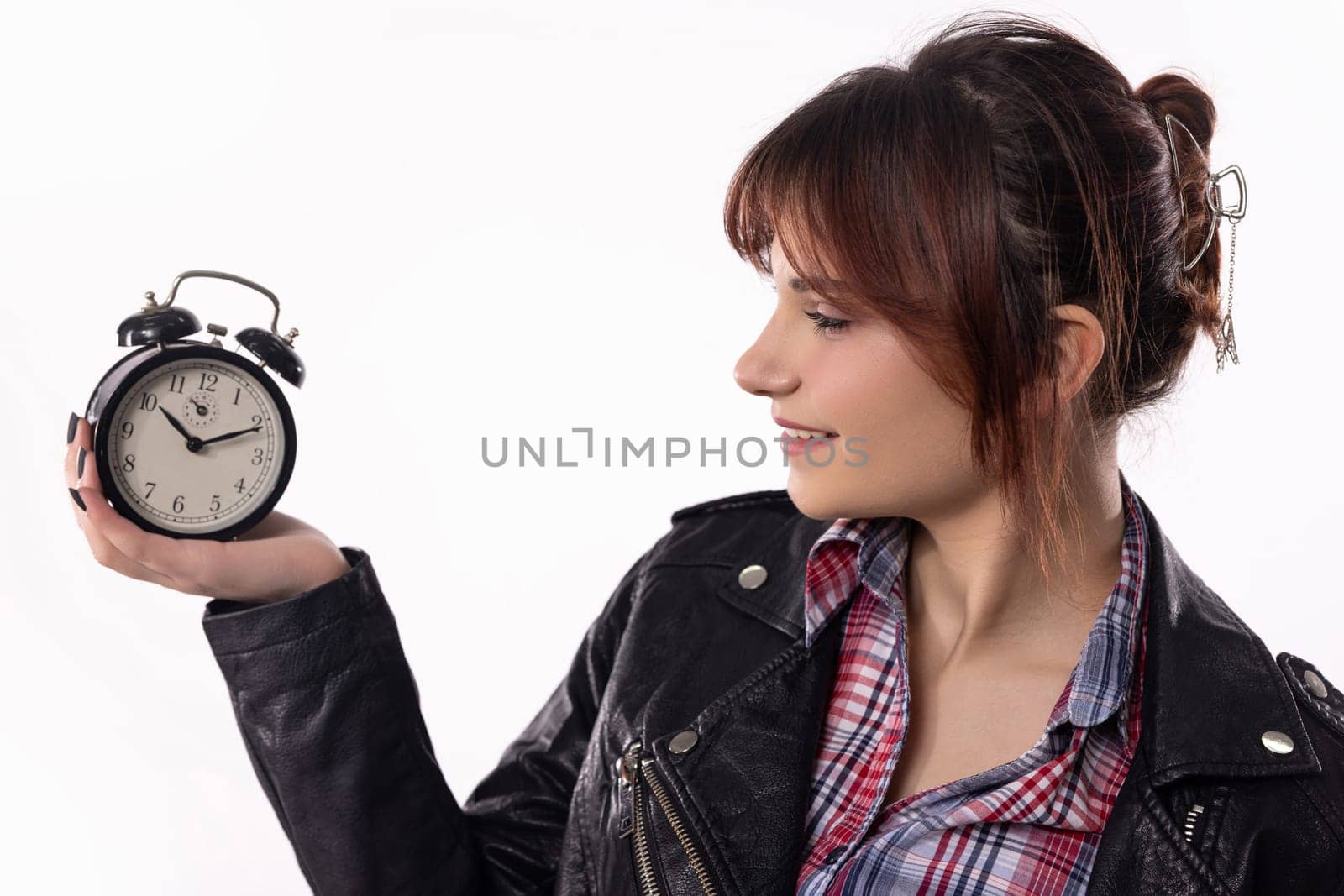 A young woman in a stylish outfit smiles while holding an alarm clock, representing time and reflection.