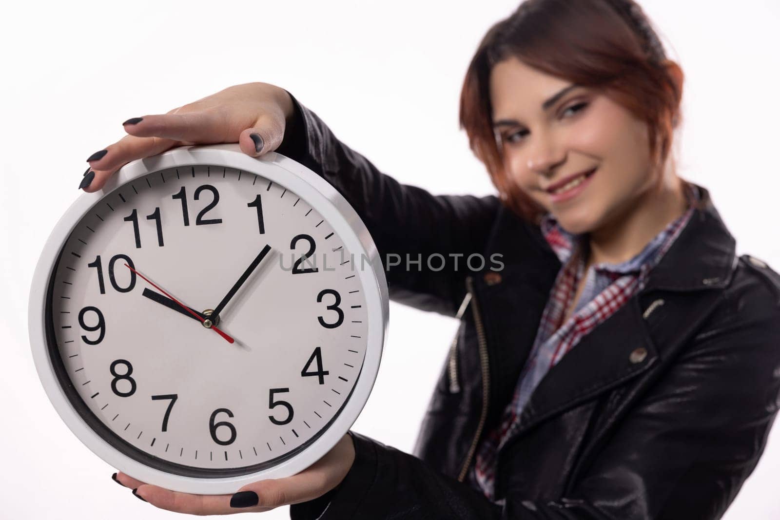 A young woman is happily smiling while holding a large clock, which is perfect for themes related to time management