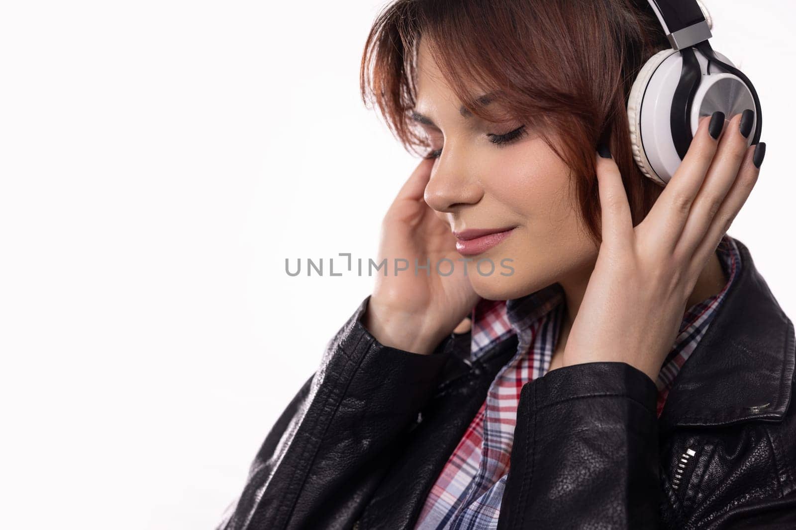 A young woman completely immersed in her music, wearing stylish headphones and a trendy leather jacket