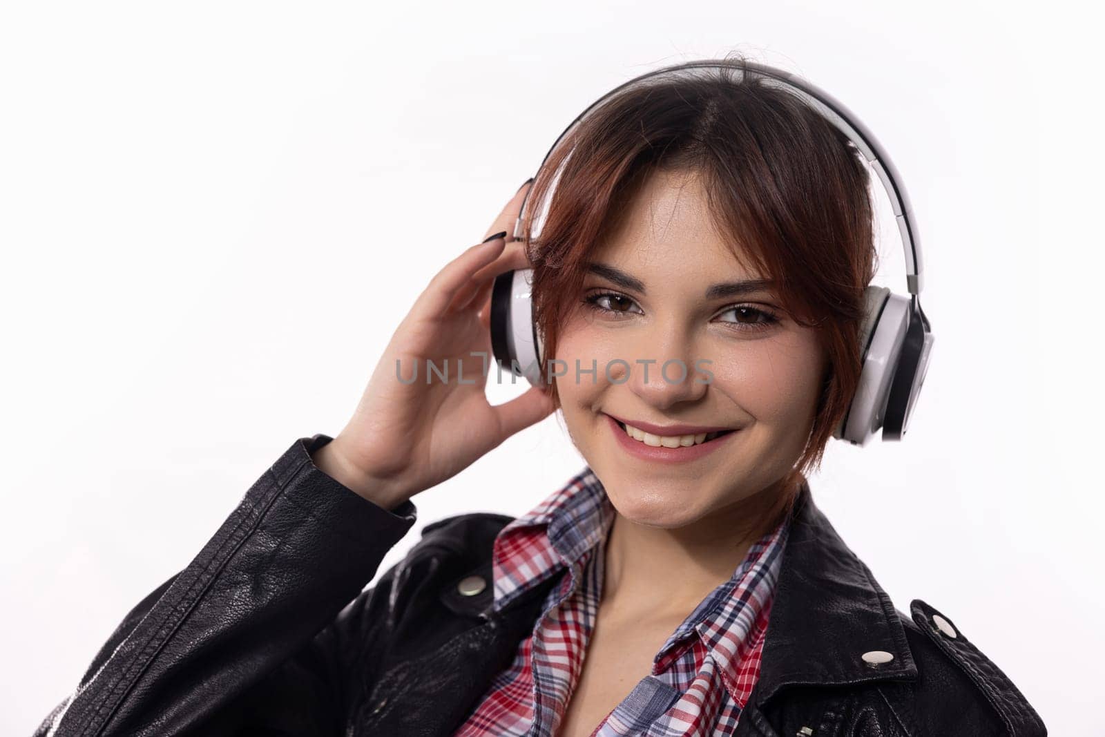 A smiling young woman, adorned with stylish headphones, relishes her music while dressed in a chic outfit