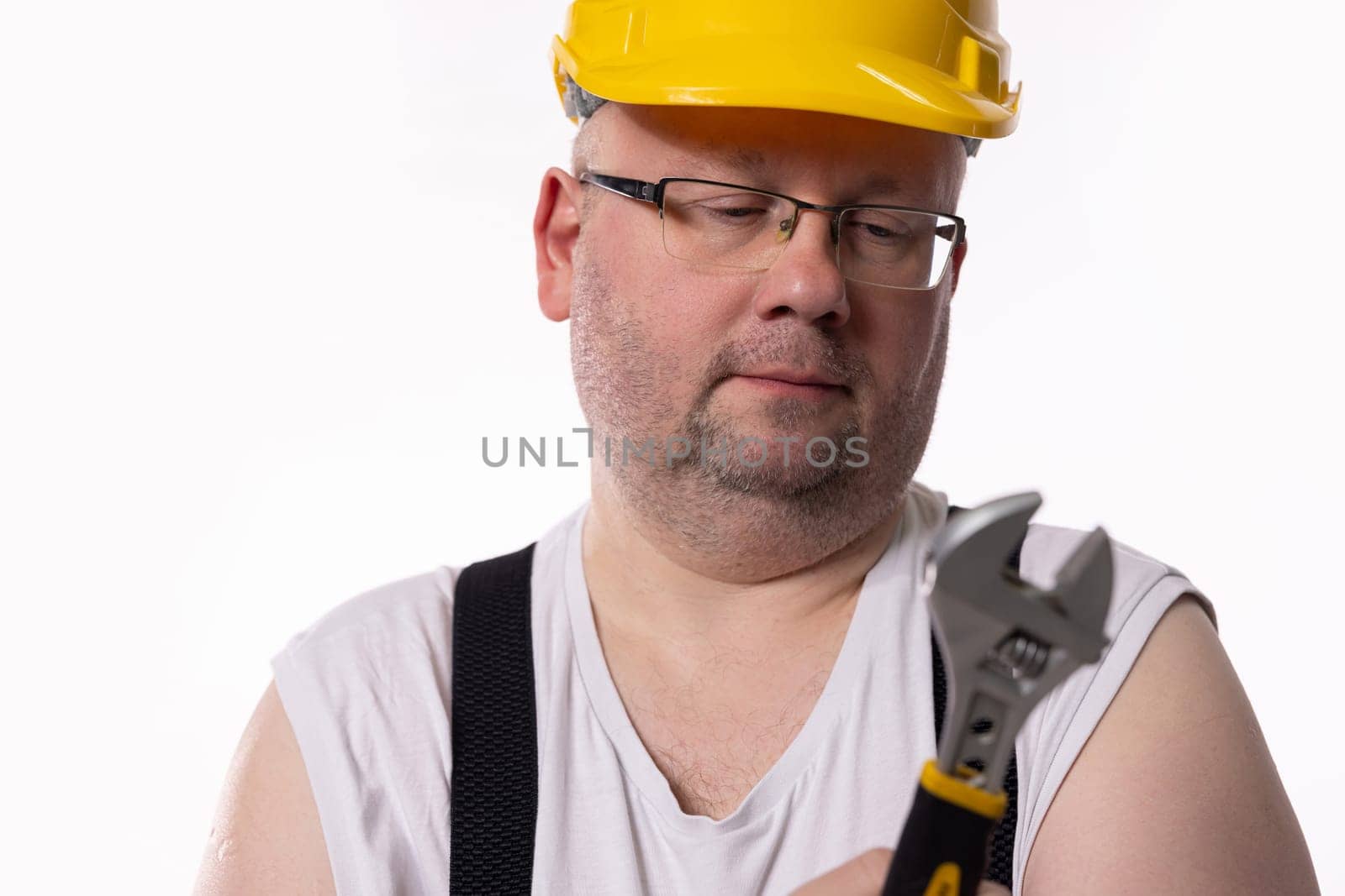 A diligent and focused construction worker carefully evaluates an adjustable wrench while wearing proper safety gear