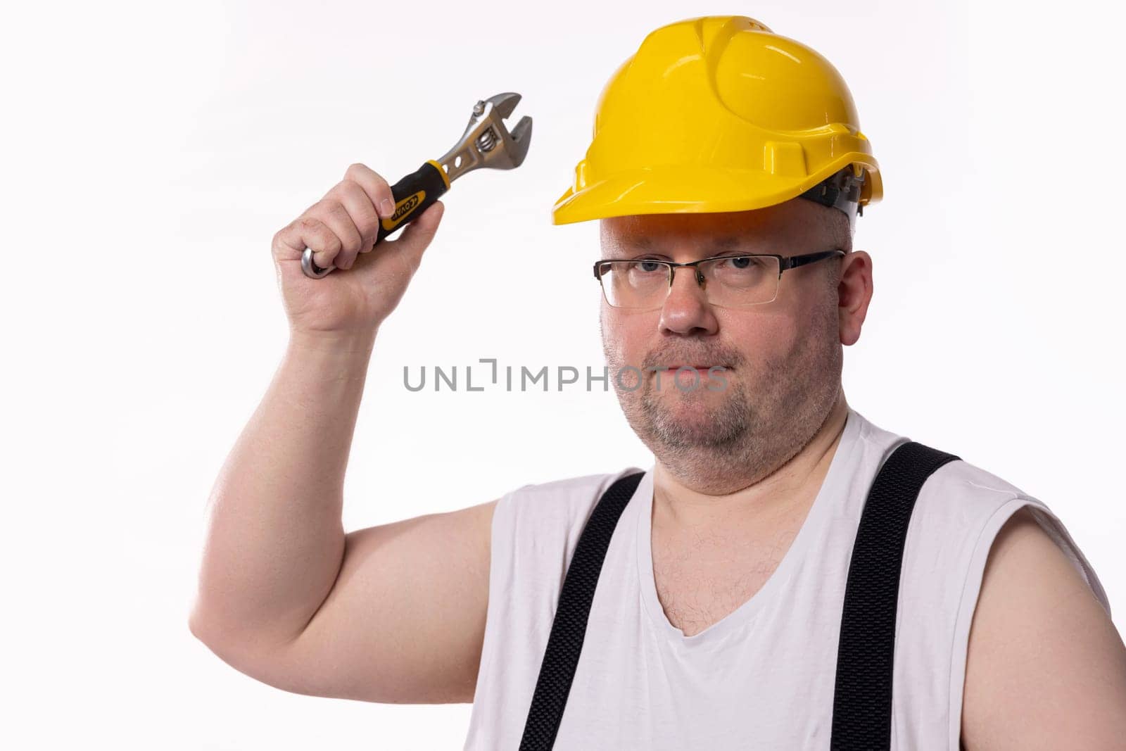 A cheerful construction worker in a yellow hard hat and tank top poses playfully with a wrench in hand