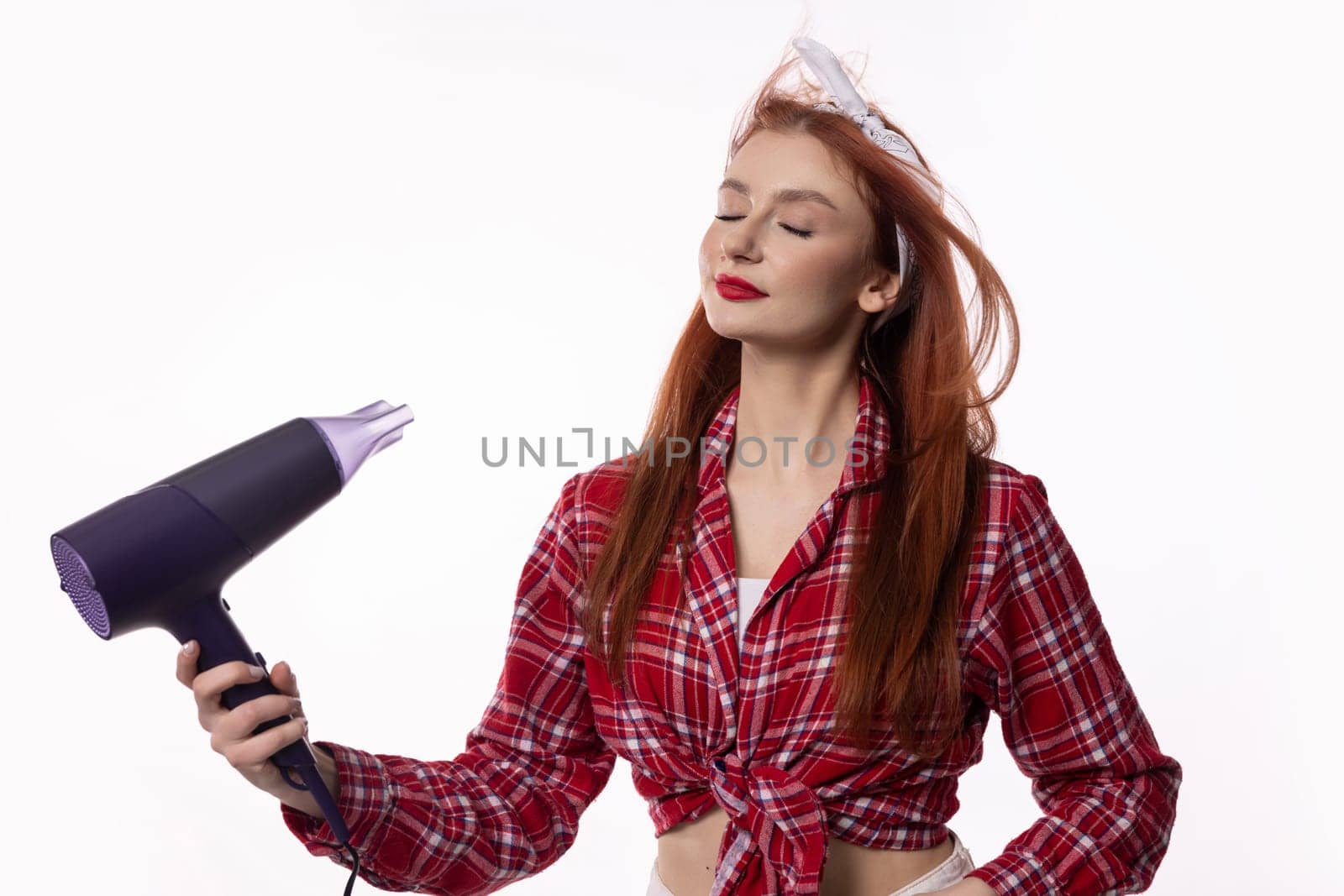 A confident redhead models stylishly with a vibrant hairdryer in chic pajamas, showcasing beauty and fun times