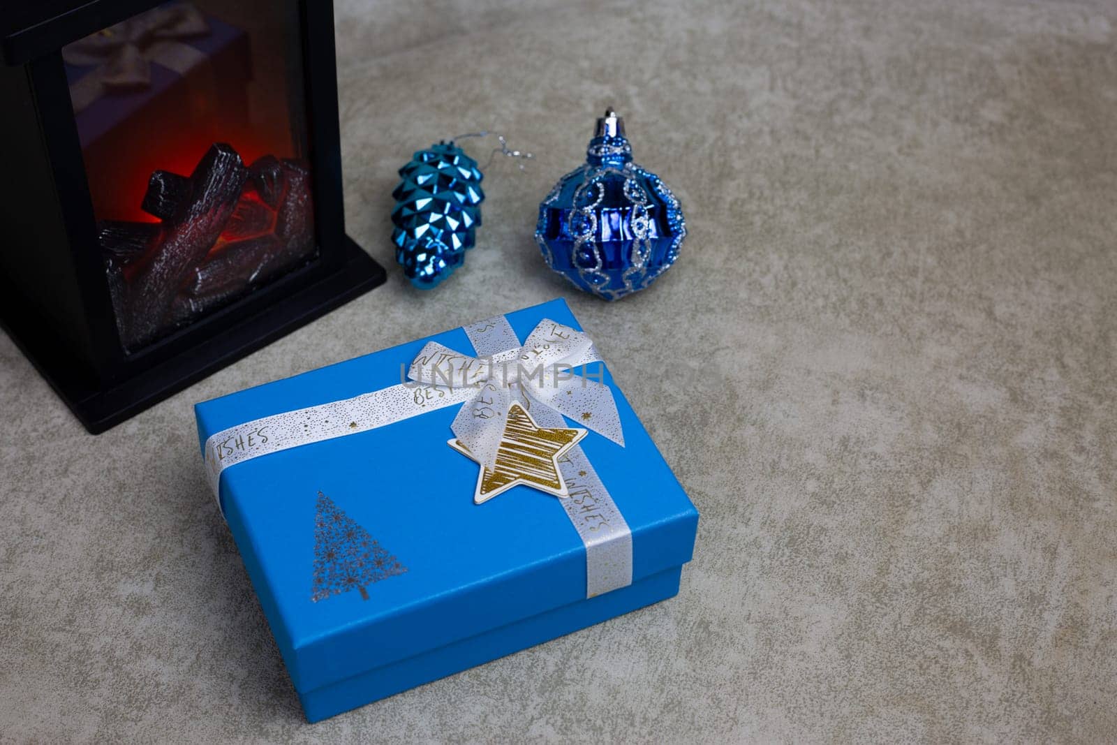 Blue gift box for the New Year, gift in beautiful package lies near decorative fireplace and Christmas toys for tree on shelf to create New Year atmosphere, Christmas gift in box with bow