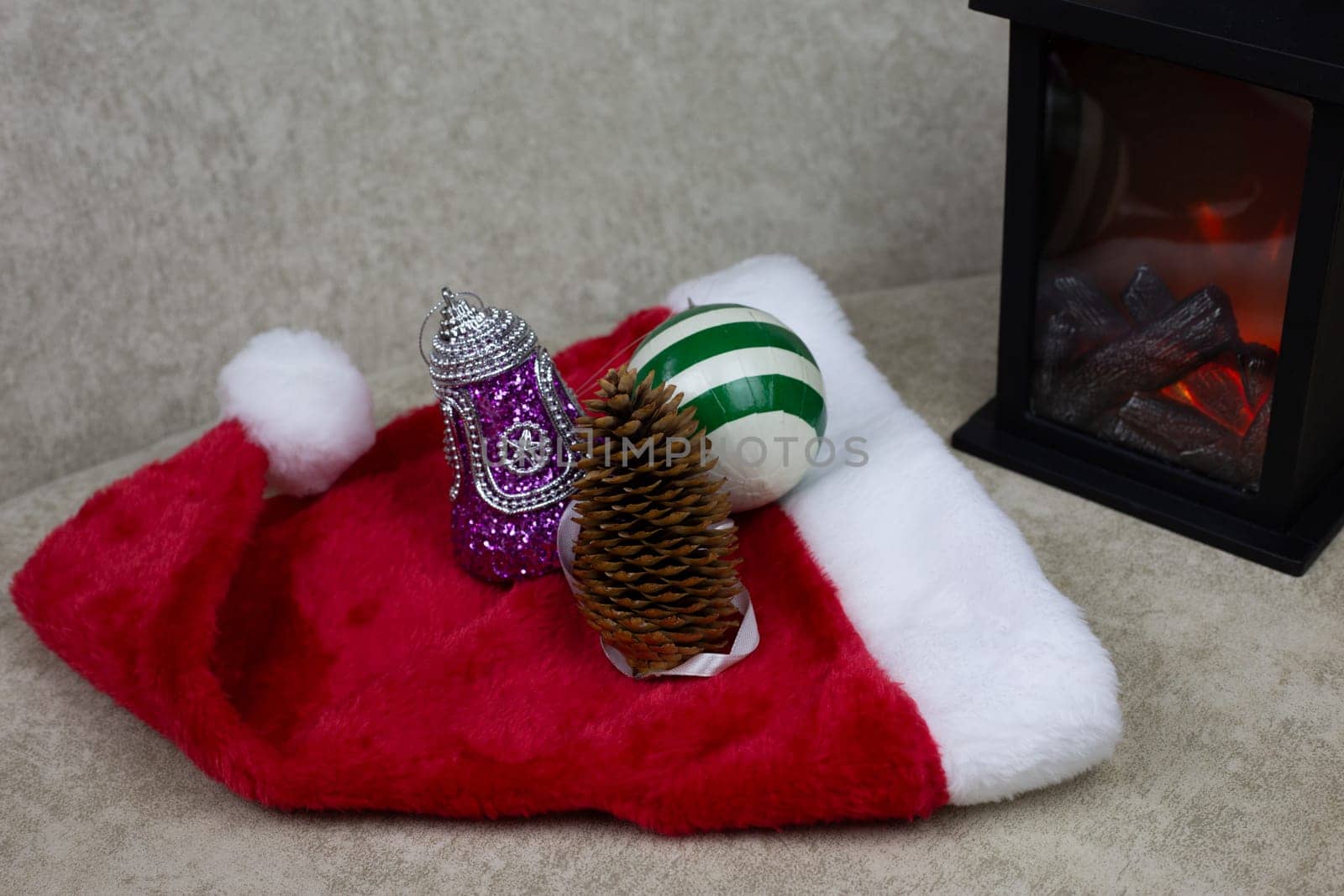 Tree cone next to Christmas toys. Decorations for New Year tree lie on red cap next to mini fireplace to create festive atmosphere, toys for happy new year and Christmas