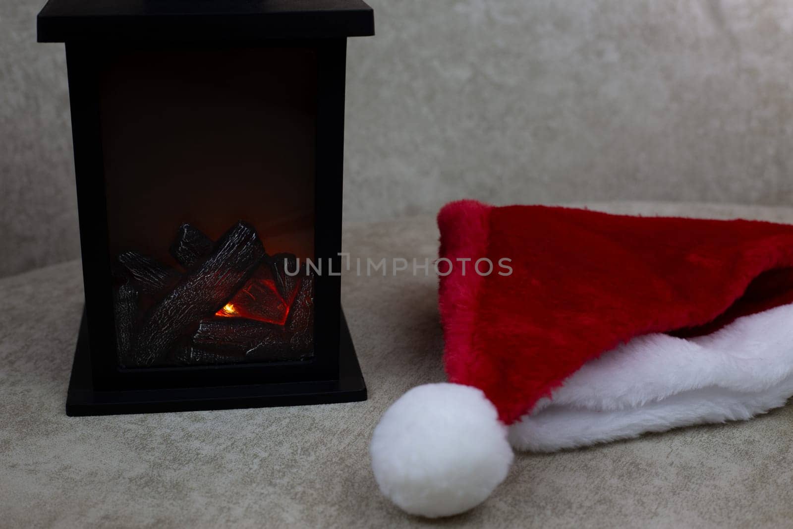 Portable fireplace for decorating interior of home for New Year against background of red cap, attributes of Christmas and New Year on light background, creating festive atmosphere