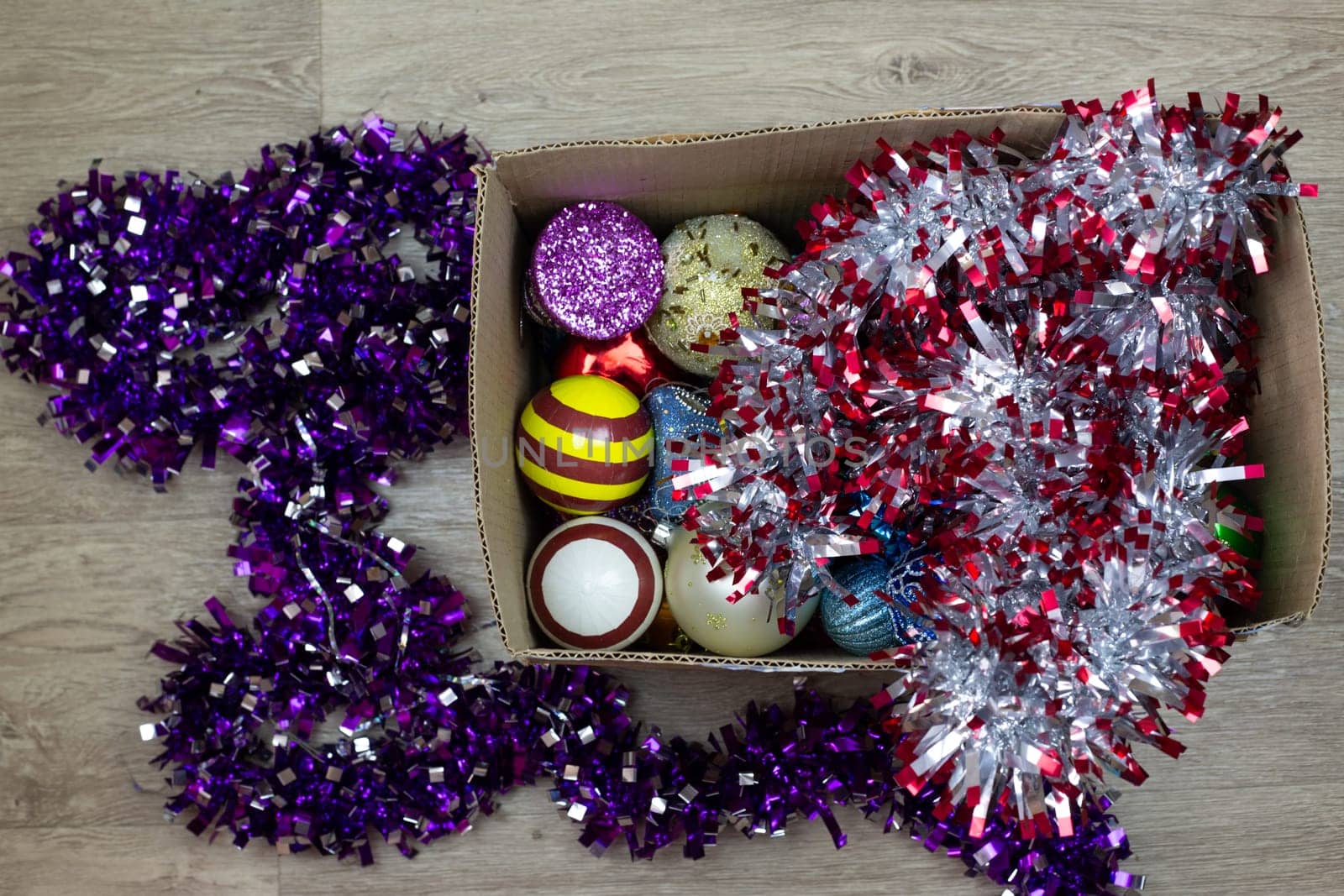 Cardboard box with New Year toys for Christmas tree and tinsel for home decoration. Top view of box of Christmas toys, preparing to decorate house and create festive atmosphere