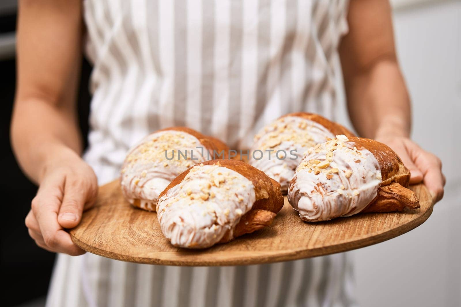 female baker holding wooden tray with freshly baked crispy golden croissants