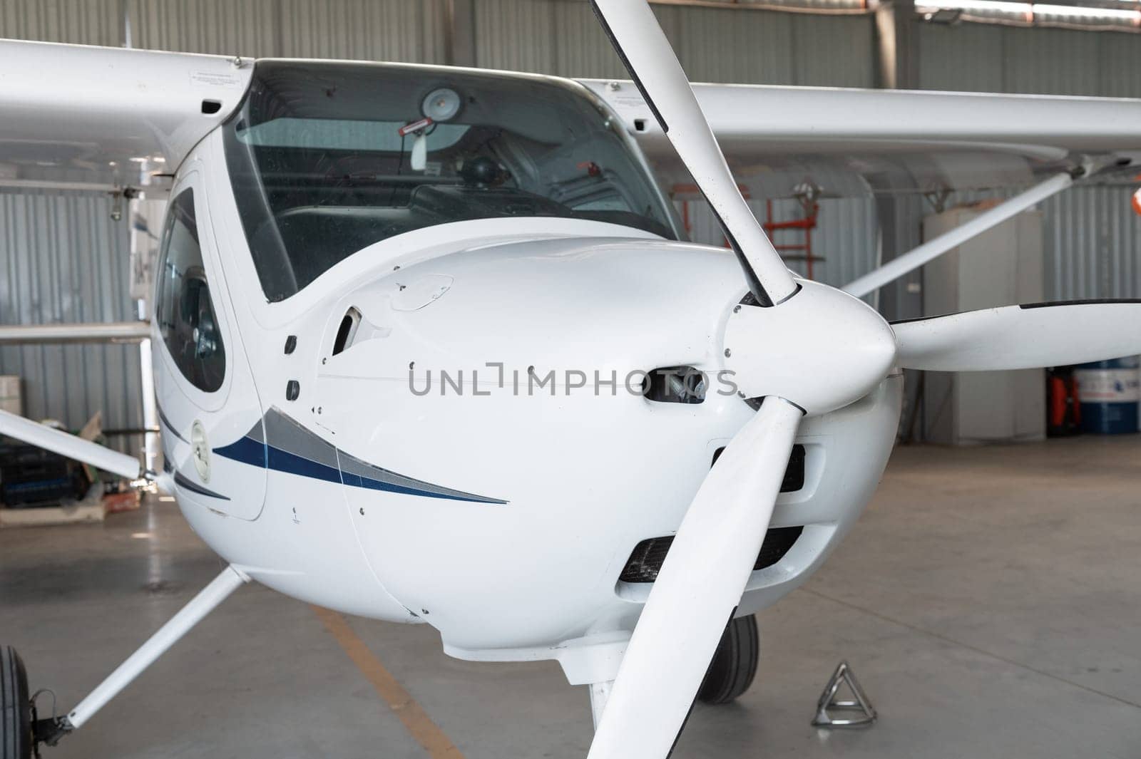 Close-up of a small white airplane with a propeller, parked in a hangar, showcasing its cockpit and wings.