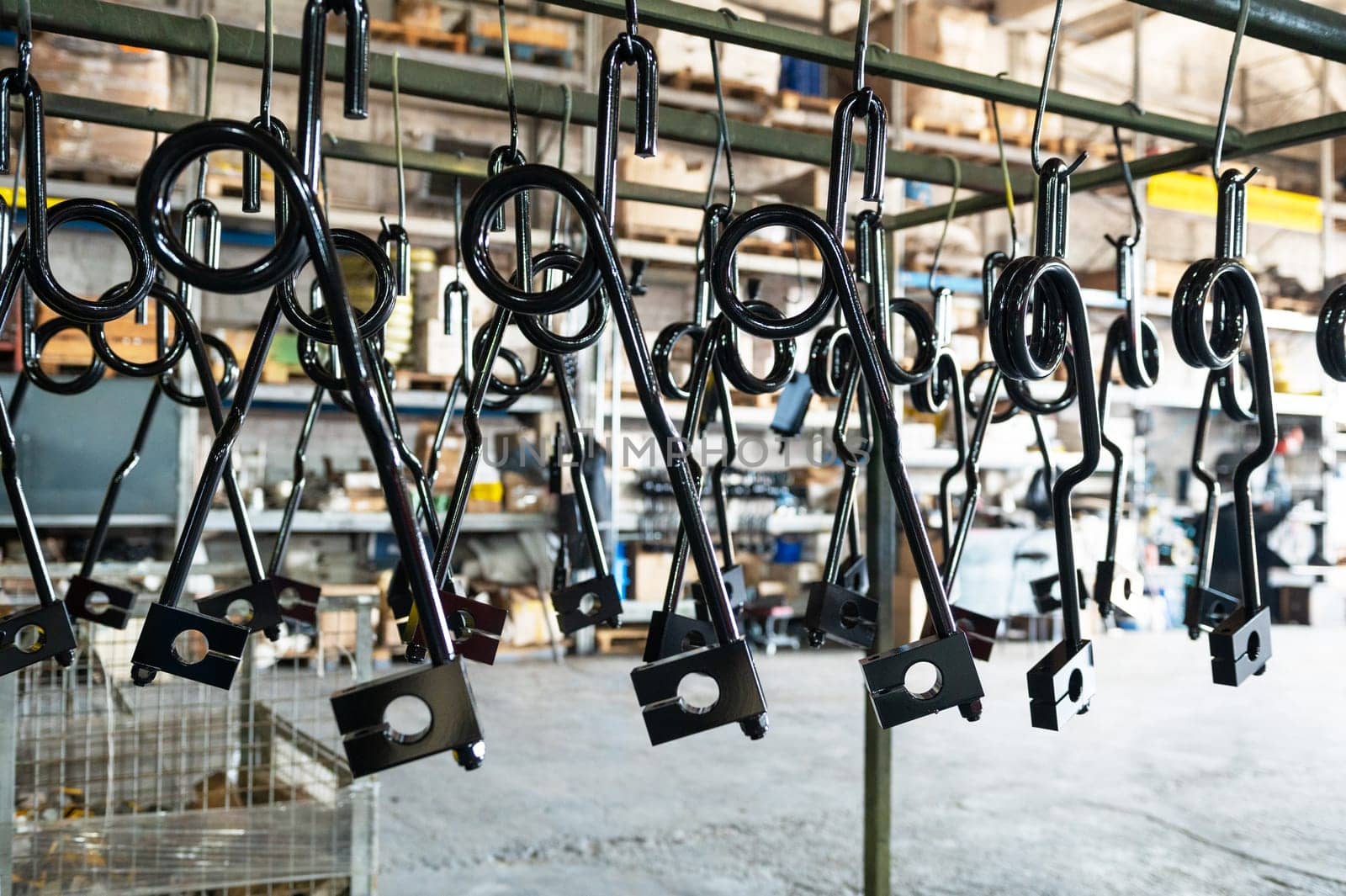 Close-up of black-coated metal parts hanging in a factory or workshop, ready for processing or assembly.