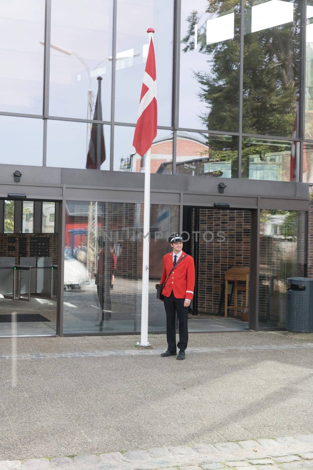 aalborg,denmark,03-09-2024: den gamly by ,A guard in a red uniform stands by the Danish flag in front of a modern building. The scene represents tradition, nationalism, and duty.