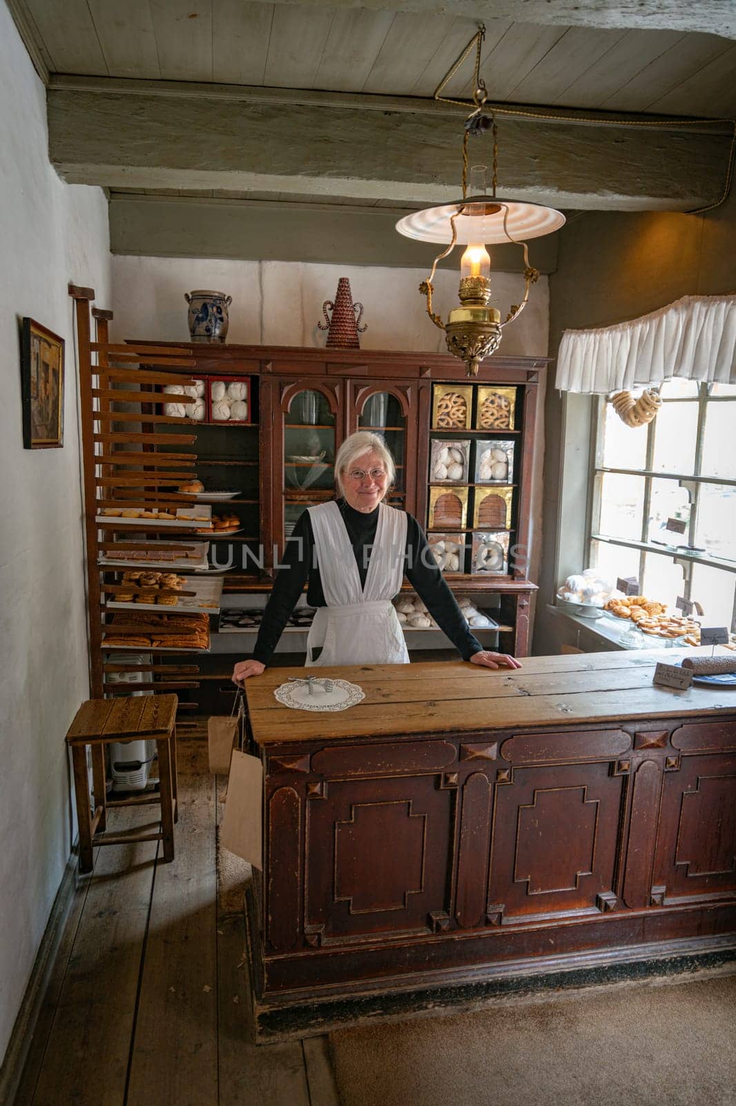 arhus,denmark,03-09-2024:A baker in a vintage bakery shop, showcasing a historical setting with wooden shelves and classic decor, conveys nostalgia and tradition. Well-lit atmosphere highlights a warm, inviting environment.