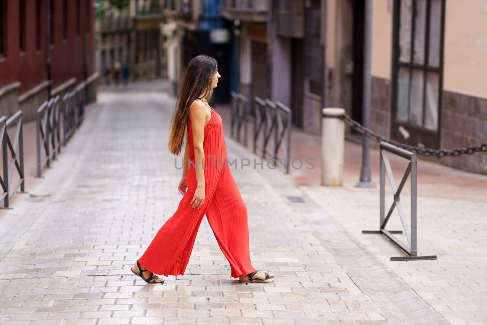 A stylish woman confidently walks on a picturesque urban street in a vibrant red dress, showcasing her unique style and selfassuredness, capturing the essence of her surroundings