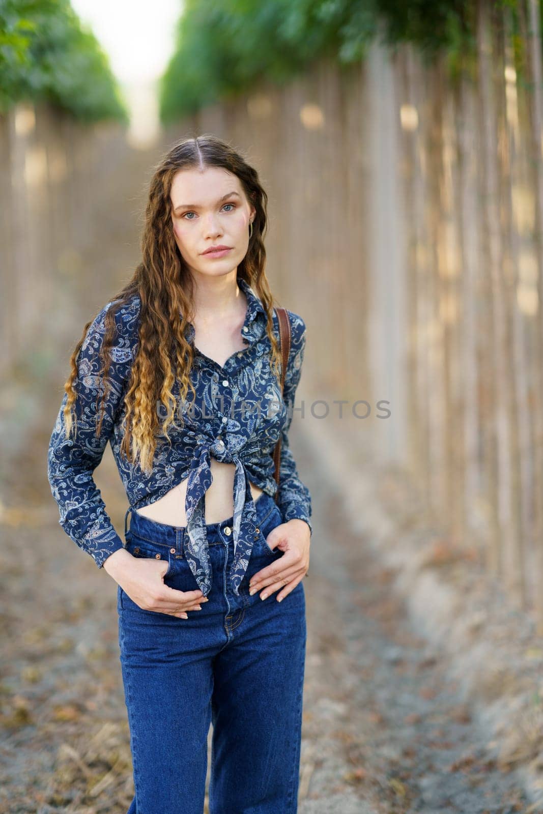 A young woman gracefully poses in a serene outdoor setting, showcasing her stylish and trendy outfit amid vibrant green surroundings, offering a picturesque scene full of life and beauty