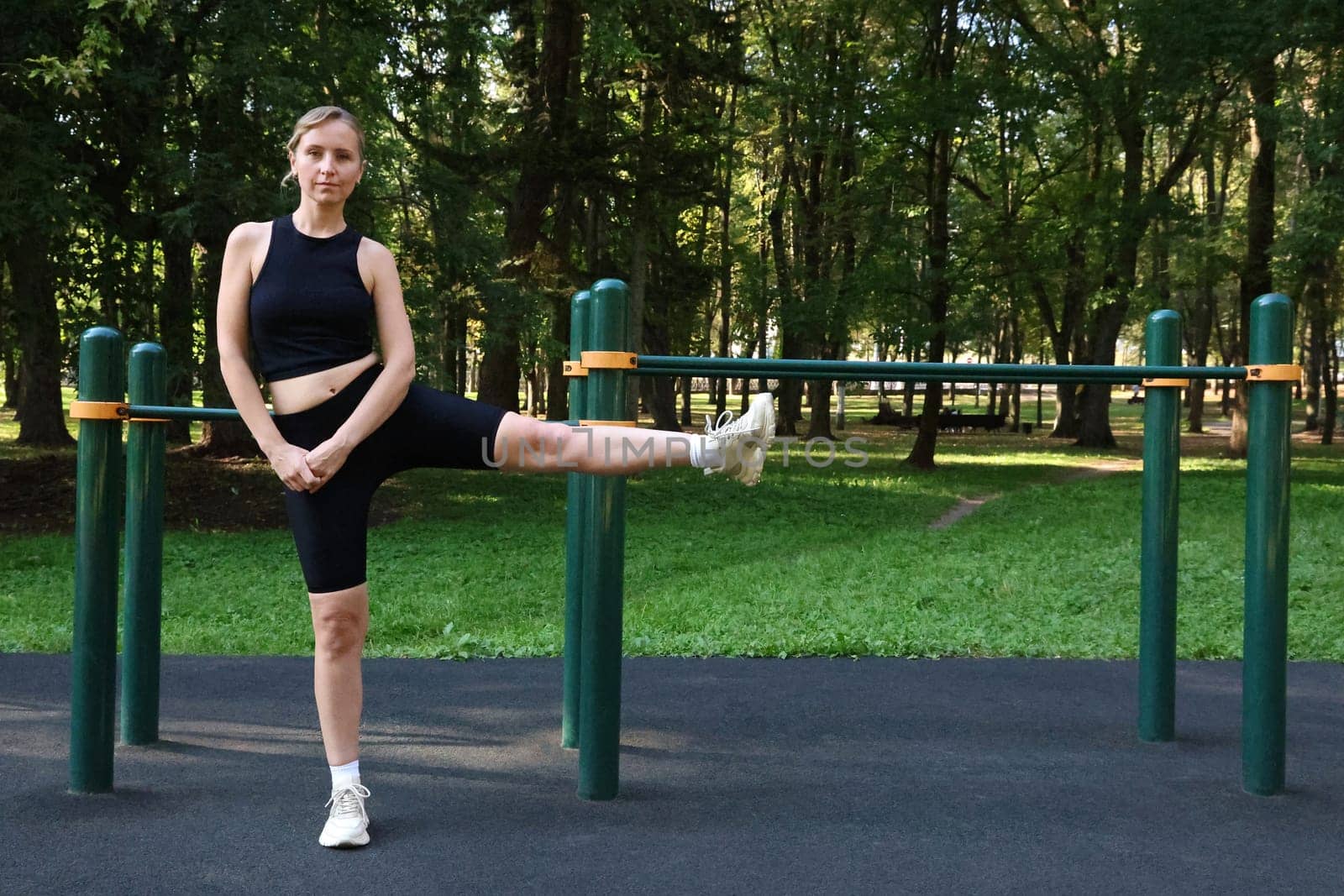 Slender woman in black sports uniform doing physical exercise against the background of sports ground. Outdoor Sports.