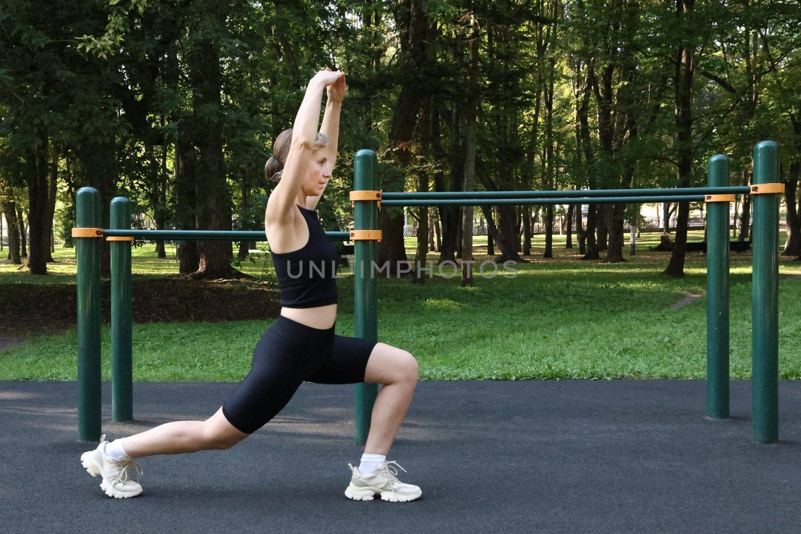 Slender woman in black sports uniform doing physical exercise on a sports ground in summer..Healthy lifestyle concept.
