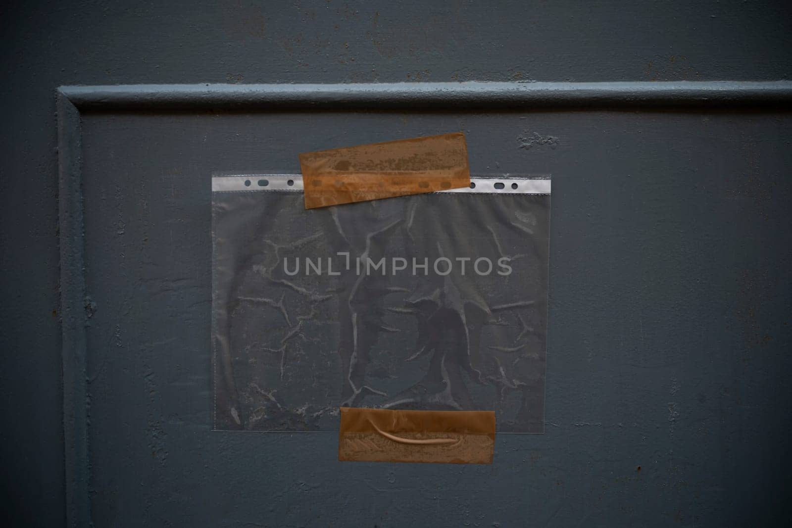 A clear plastic sheet is hanging on a grey wall with pieces of adhesive tape, creating a textured and minimalist background