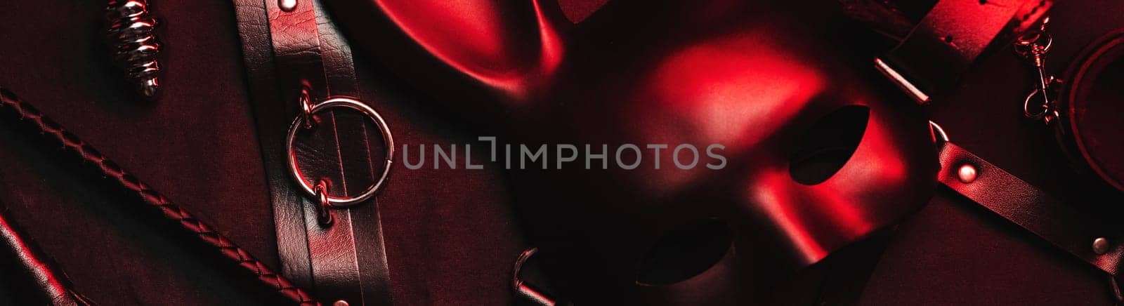Set of erotic toys from a sex shop on a black and red background. Mask, leather belt, choker, handcuffs, whip and anal plug. Panoramic wide horizontal photo for banner head cover