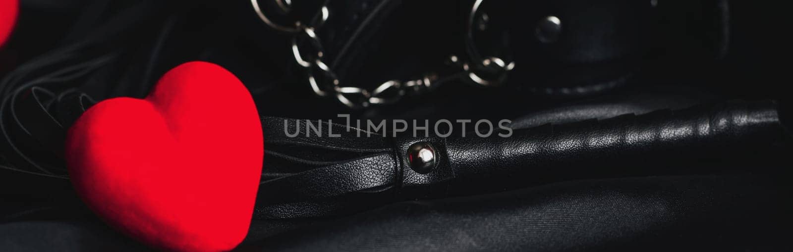 Leather whip and handcuffs for BDSM sex with red hearts as a symbol of Valentine's day holiday with love and sex with submission. Panoramic wide horizontal photo for banner head cover