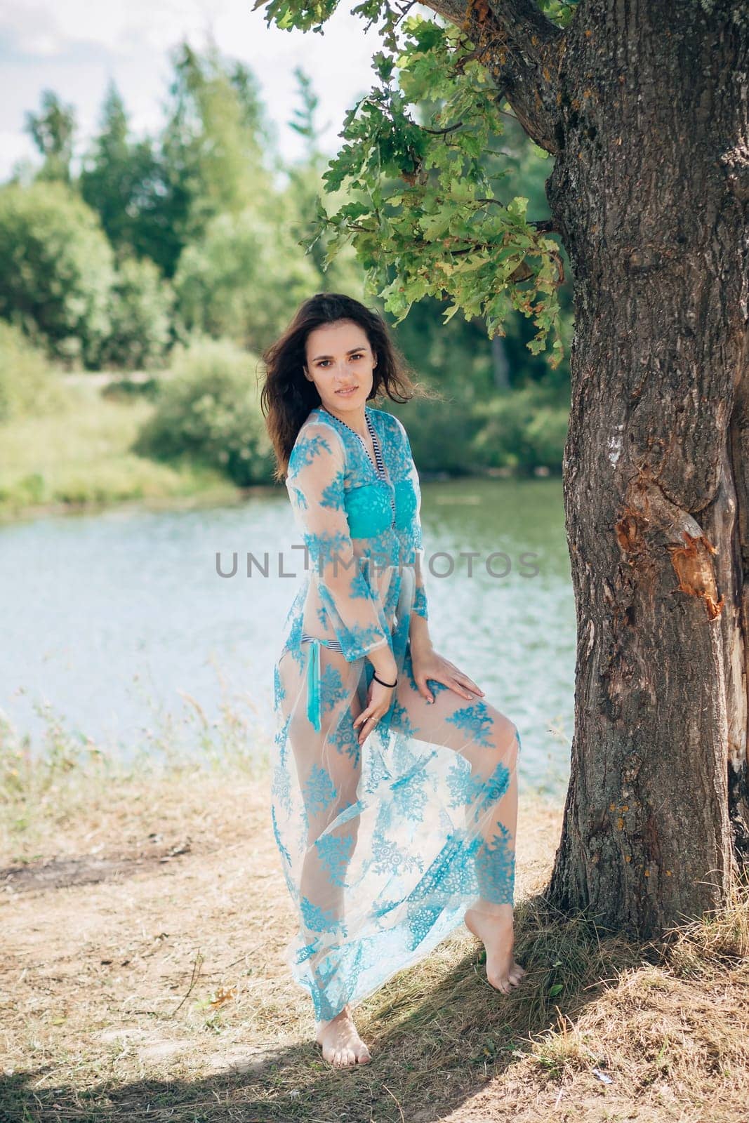 young girl with a sexy body in swimsuit and tunic poses on beach by river in summer