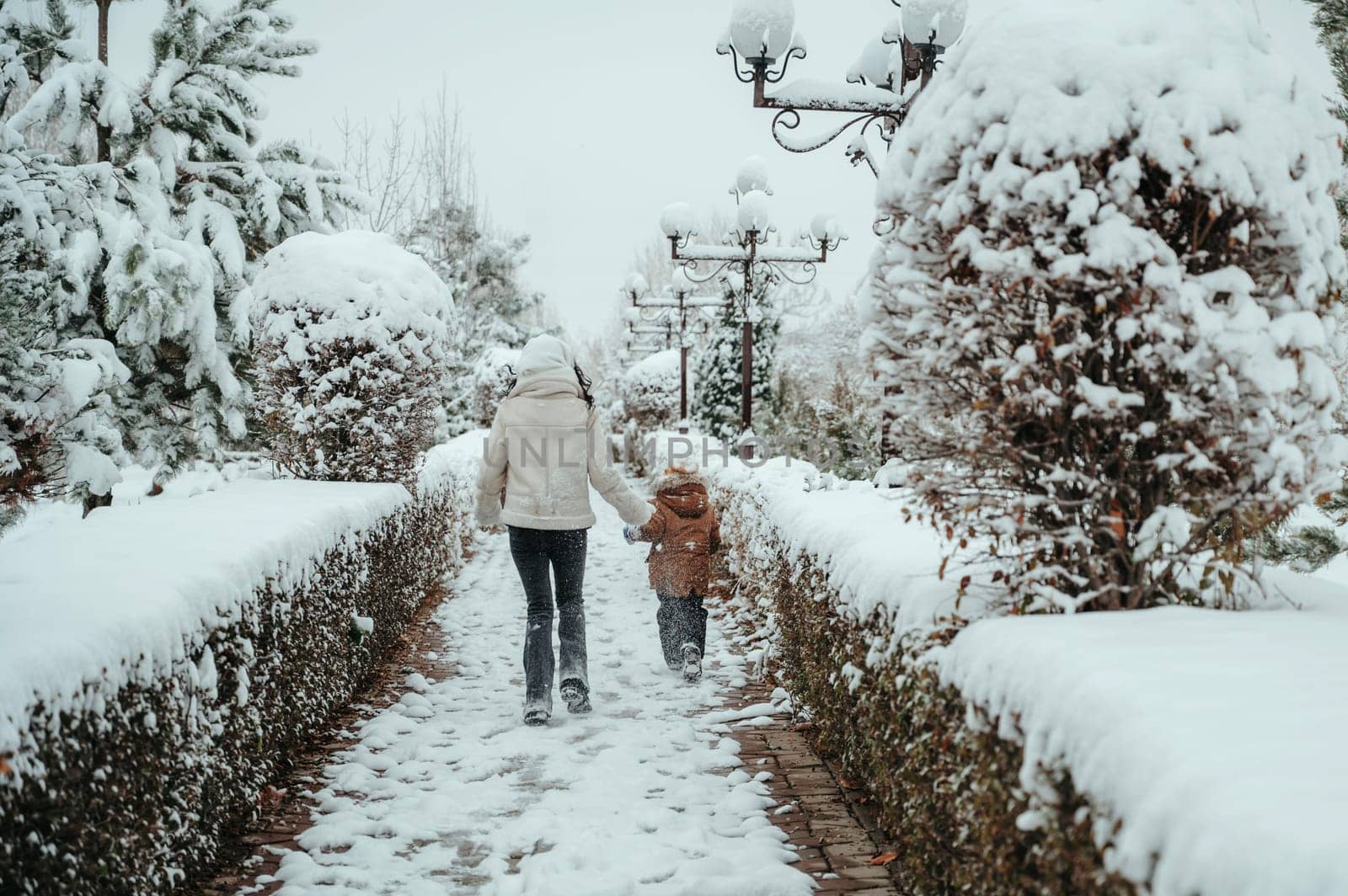 Happy cheerful mom with a child boy and son running backs in the snow in winter in the park