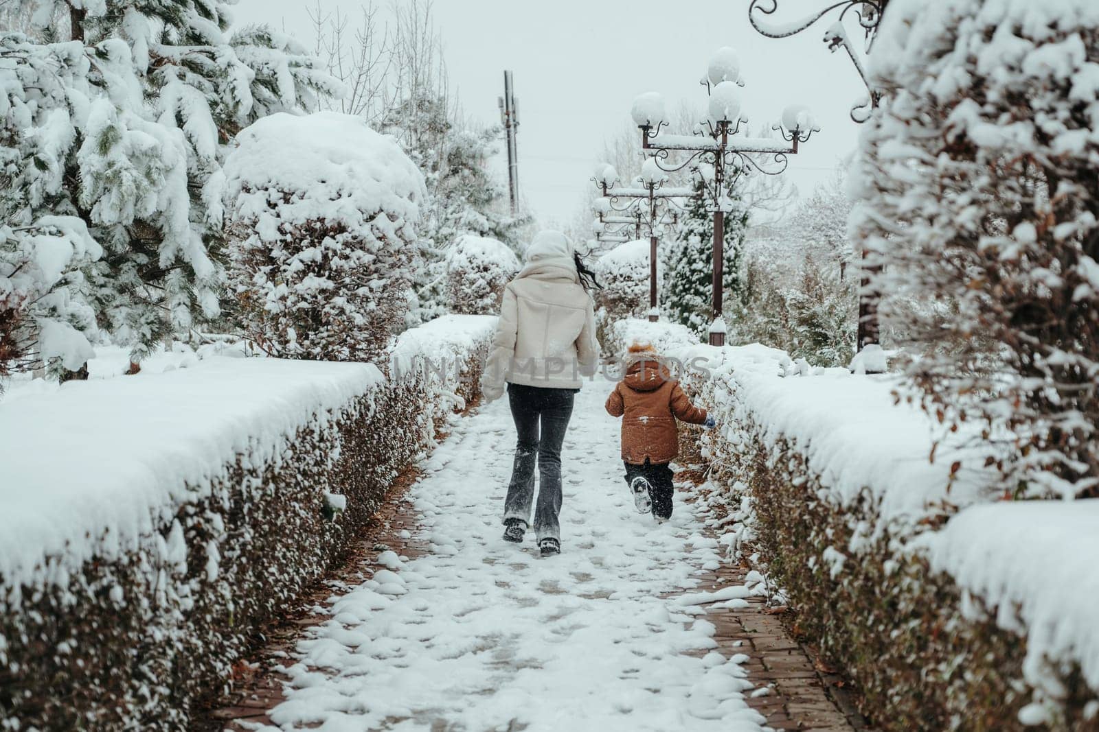 Happy cheerful mom with a child boy and son running backs in the snow in winter in the park