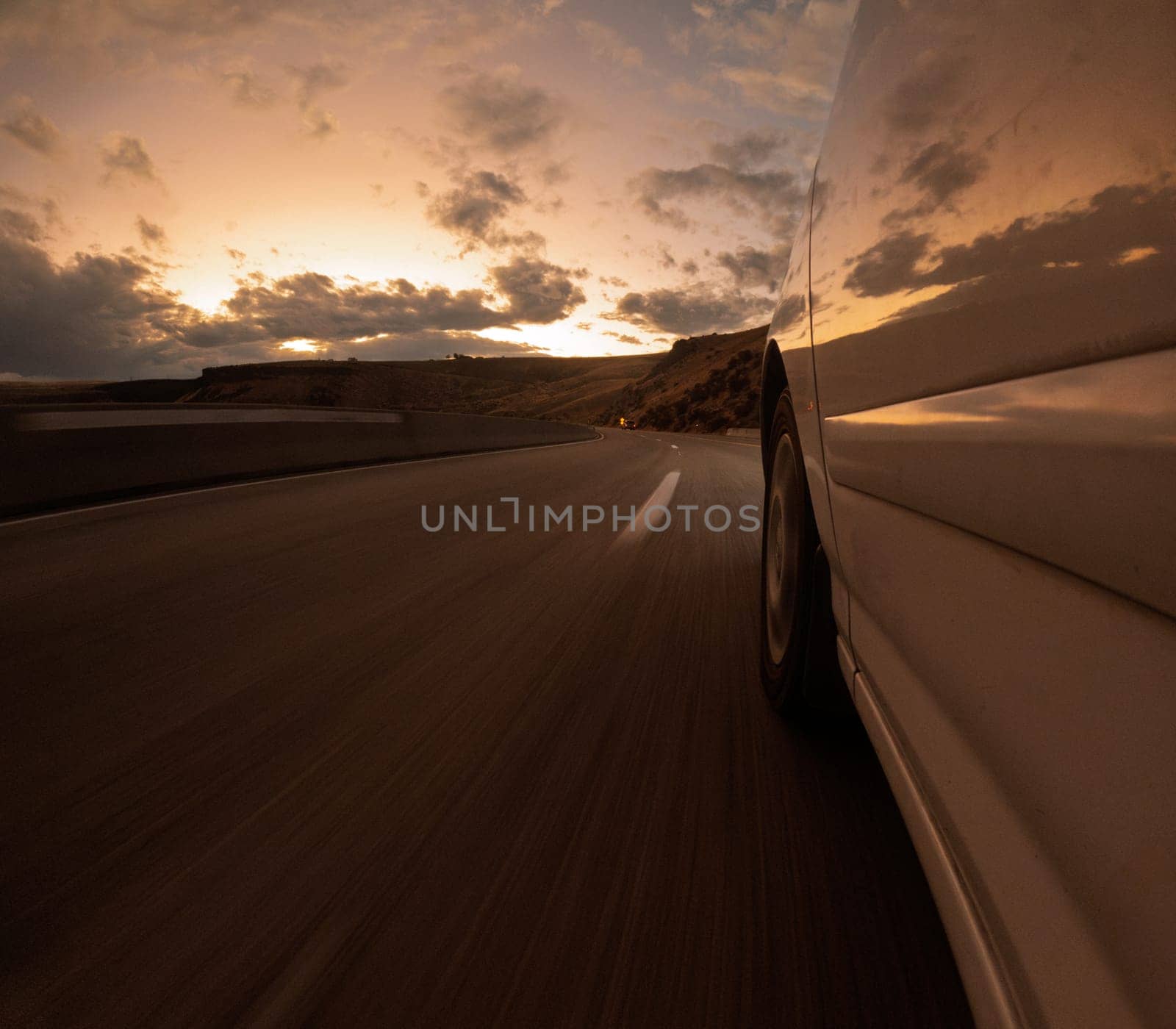 A car travels along an open road under a dramatic sunset sky, embodying freedom and adventure. The scene captures the essence of travel with a sense of motion and tranquility.