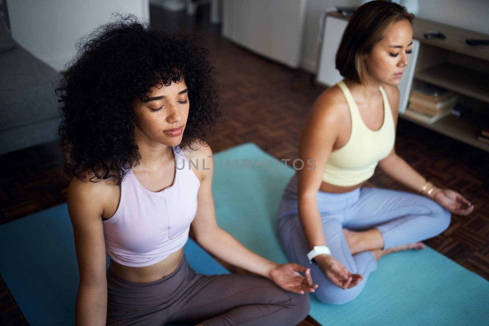 Pilates, fitness and girl friends in the living room doing a meditation in lotus position together. Calm, peace and young women doing yoga workout or exercise for breathing in the lounge at apartment by YuriArcurs