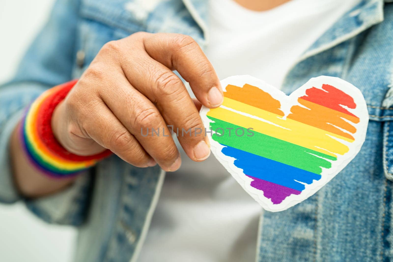 Asian lady wearing rainbow flag wristbands and hold red heart, symbol of LGBT pride month celebrate annual in June social of gay, lesbian, bisexual, transgender, human rights. by pamai