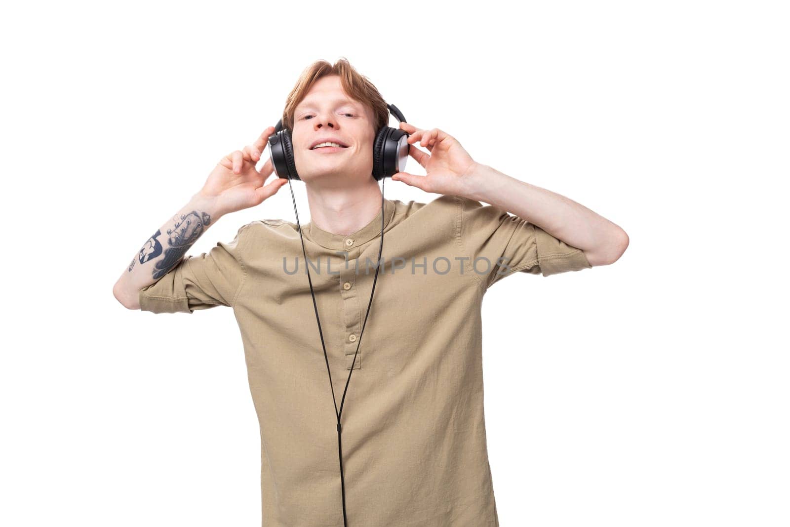young handsome red-haired man student man listens to music in big wired headphones by TRMK