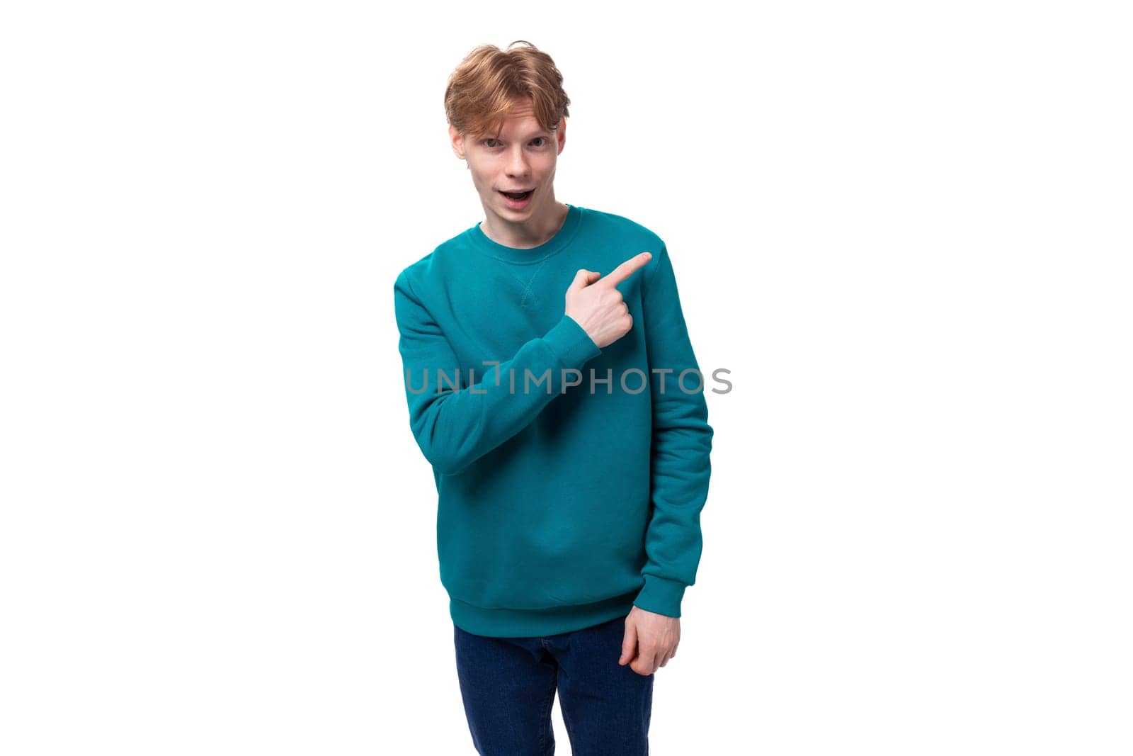 surprised caucasian young red-haired guy dressed in a blue pullover on a white background with copy space.