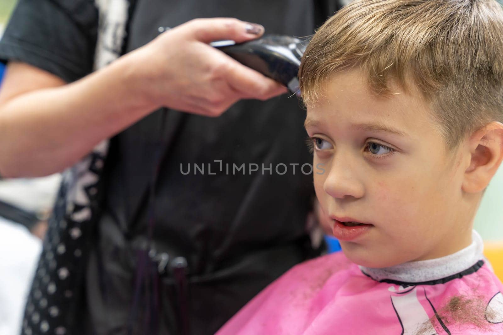 Hair cutting for a child using a hair clipper in a beauty salon. a school-age boy gets a haircut at a barber shop. a Caucasian boy in a beauty salon makes a stylish hairstyle