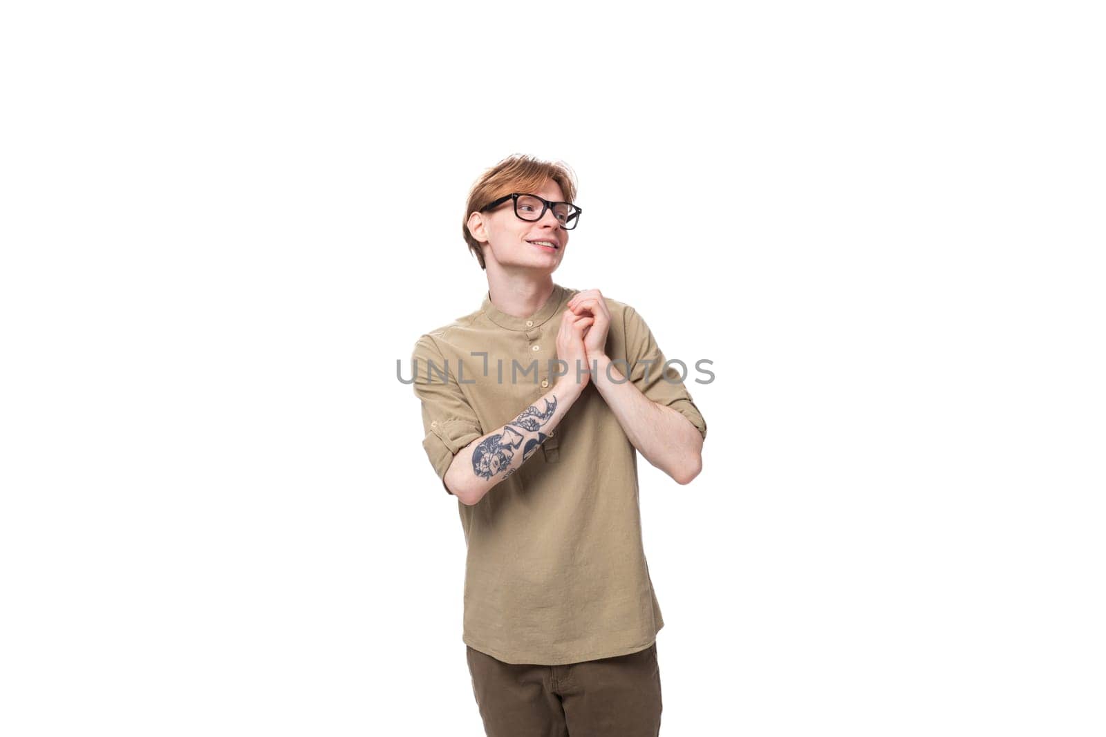 smart young red-haired man in a beige shirt wears eyeglasses on a white background.
