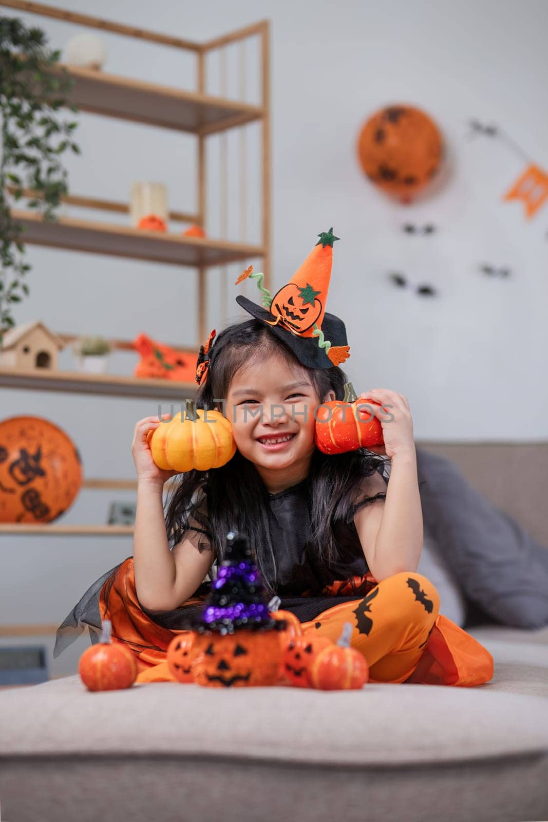 Cute little girl wearing a Halloween costume holding a pumpkin at home with happy eyes. looking at the camera. by wichayada