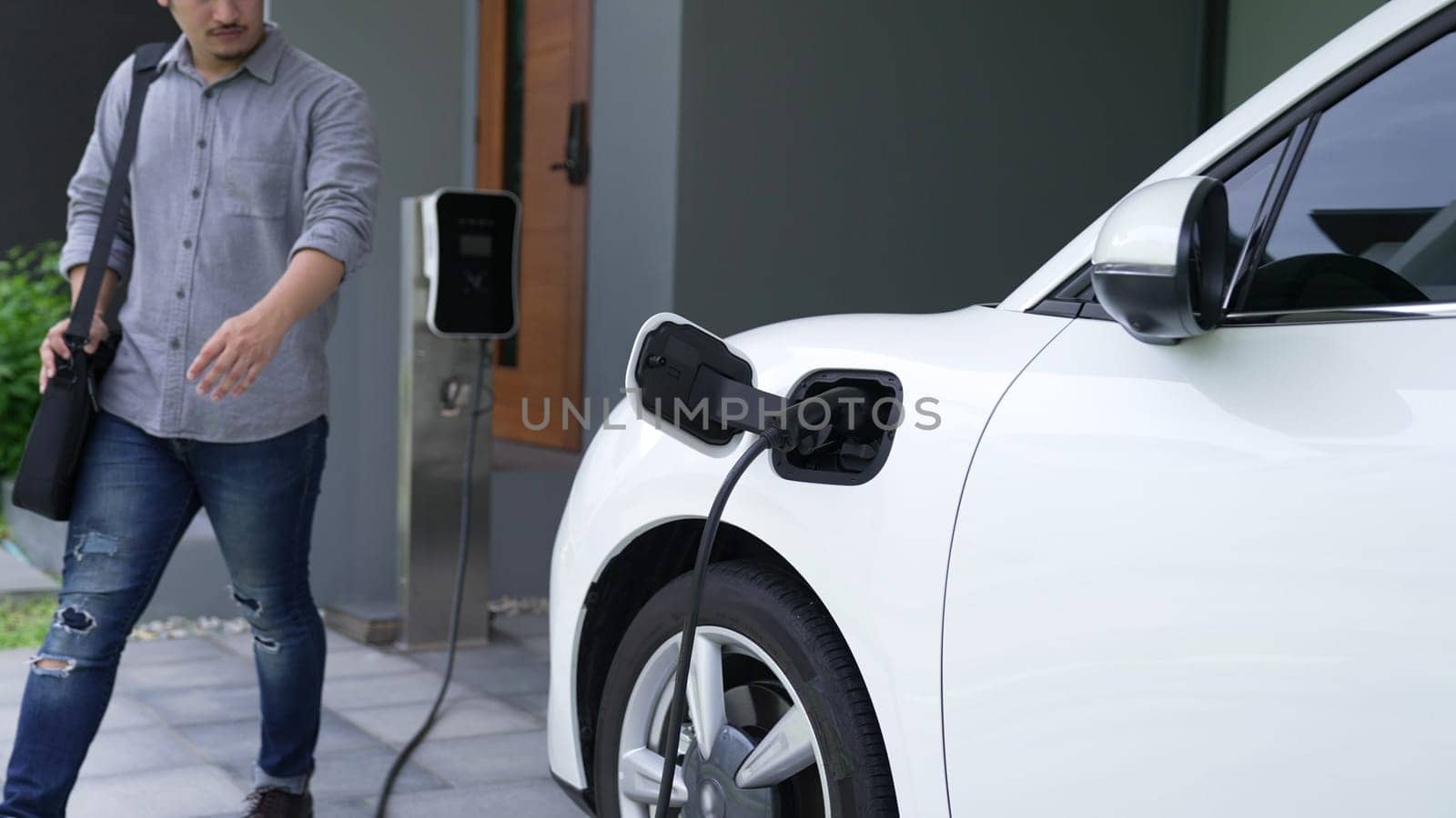 Progressive man unplugs the electric vehicle's charger at his residence. by biancoblue