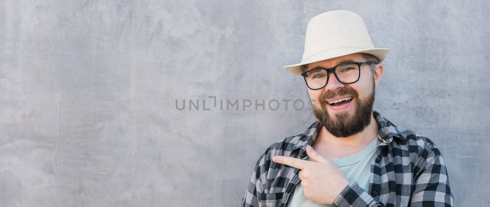 Banner man tourist looking happy wearing straw hat for travelling and pointing on empty space, standing against concrete wall background with copy space by Satura86