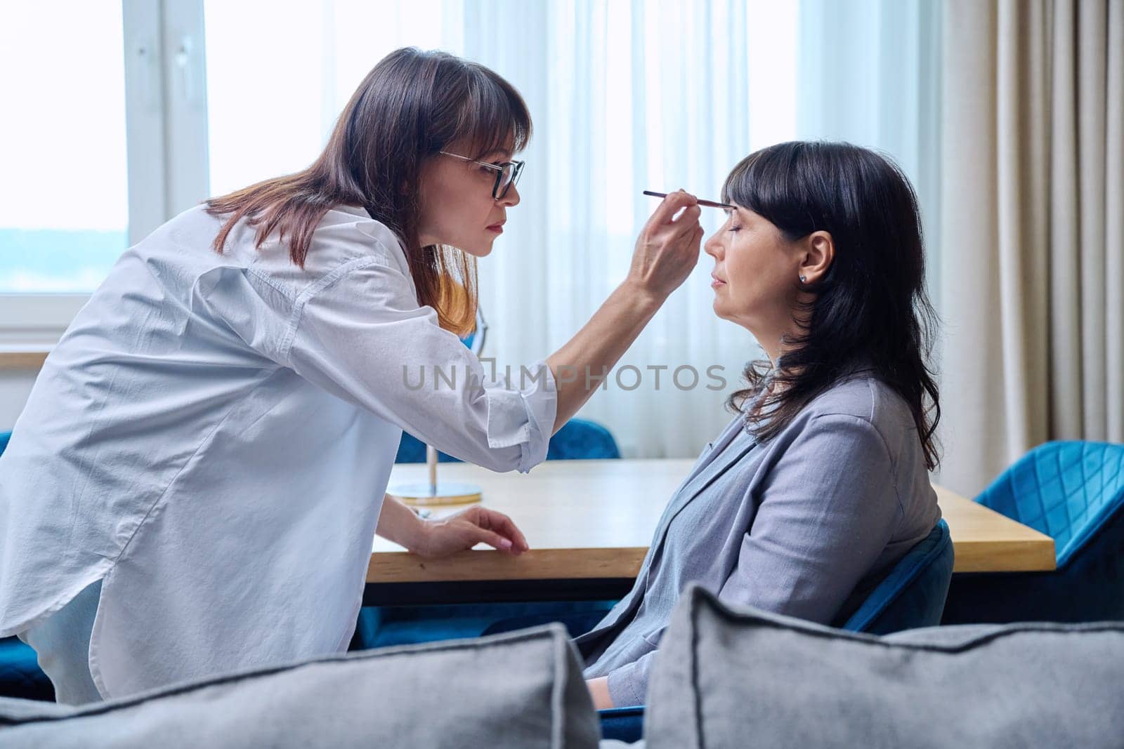 Makeup artist doing makeup for a mature business woman. Beauty, cosmetics, care, face, 50 years old woman