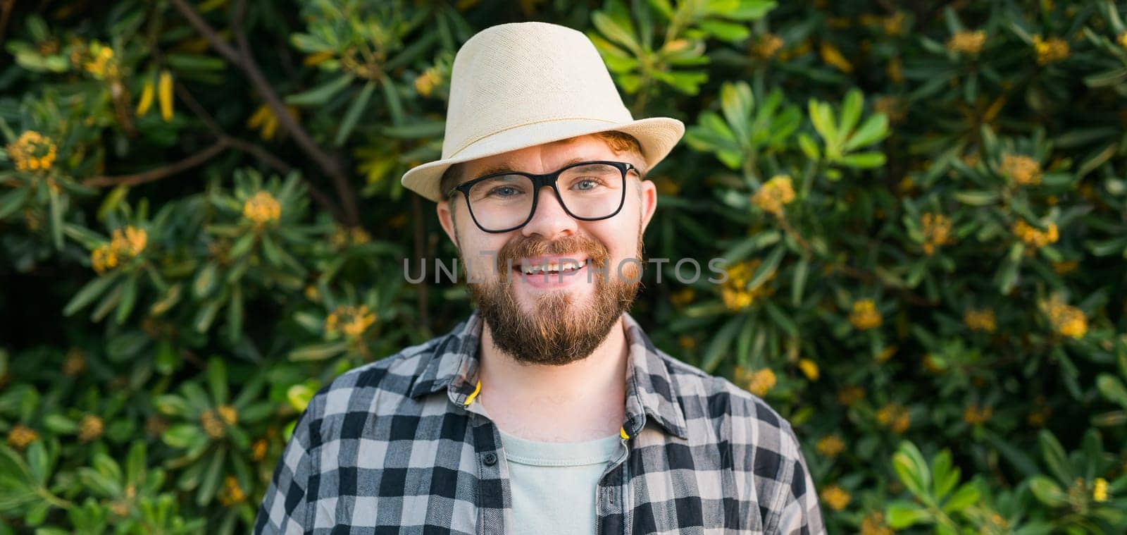 Laughing attractive man wearing hat over green tree background - emotion and vacation travel holidays