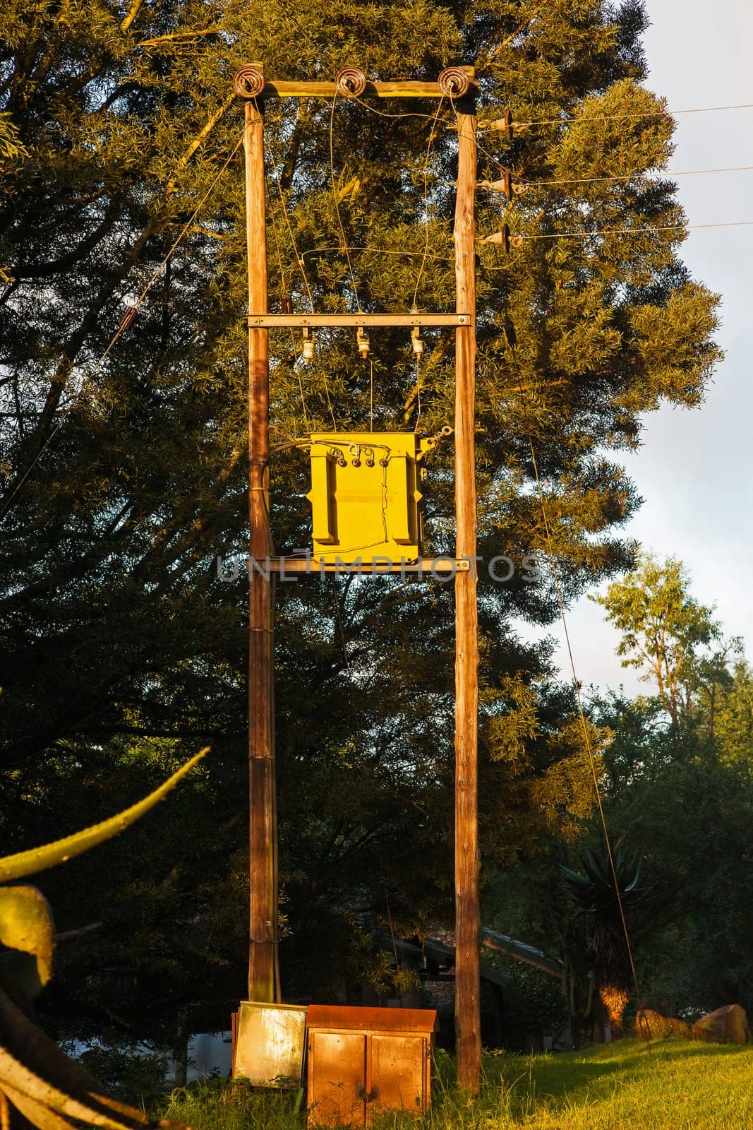 Overhead electrical distribution line with a transformer box on double wooden poles.