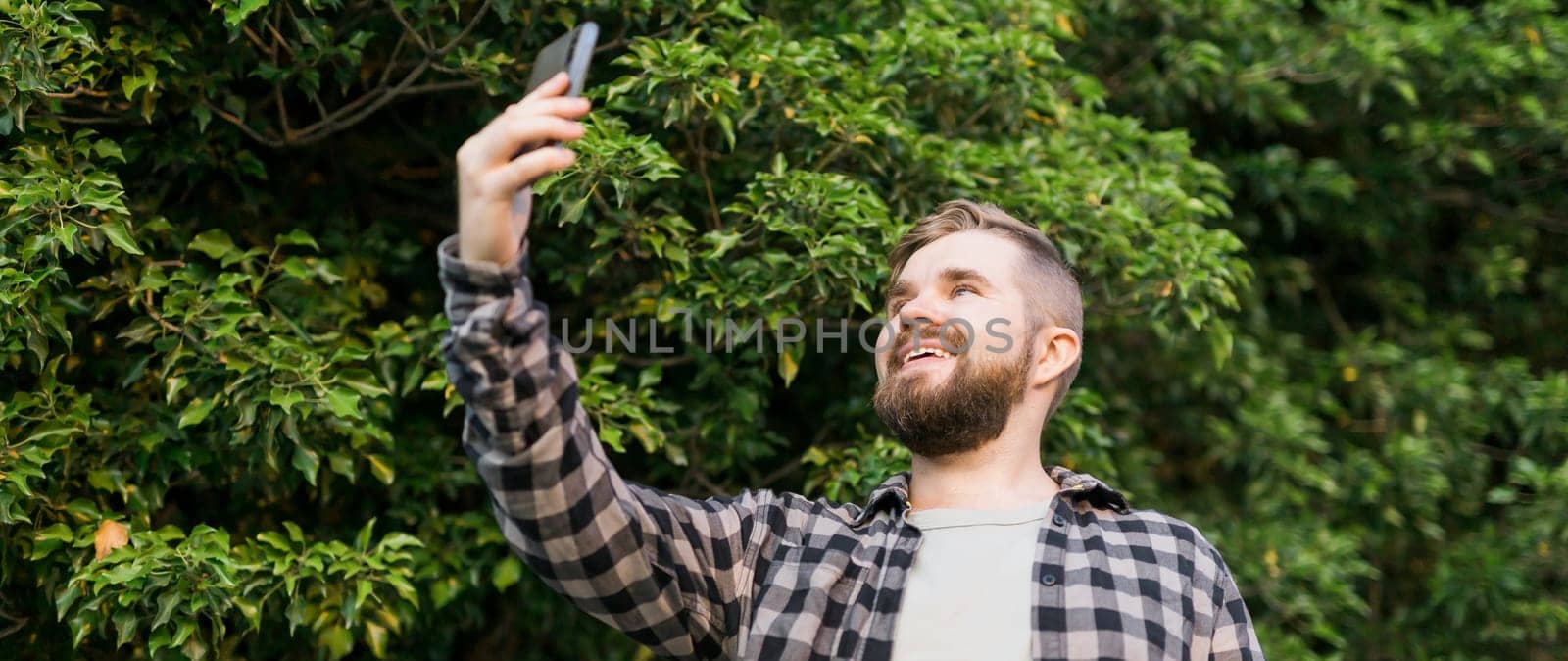 Banner man taking selfie portrait over tree background - Happy millennial guy enjoying summer holidays in city - Youth and technologies. Banner by Satura86