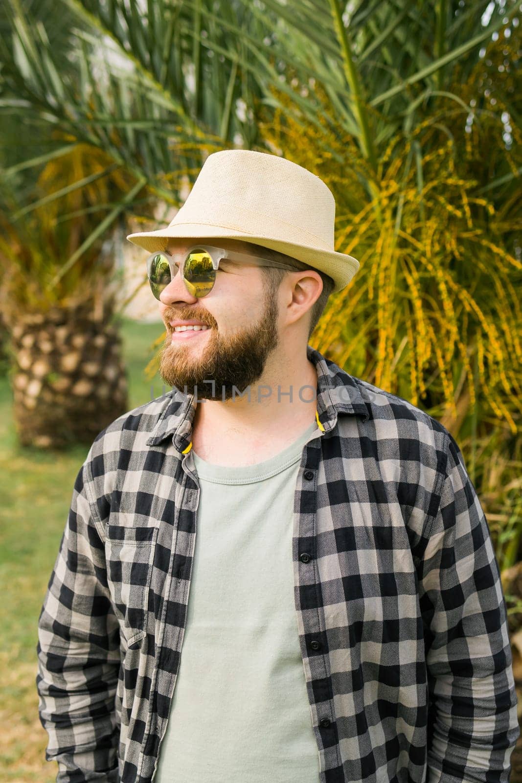 Laughing millennial man wearing hat over palm tree background with copy space - emotion and vacation travel holidays