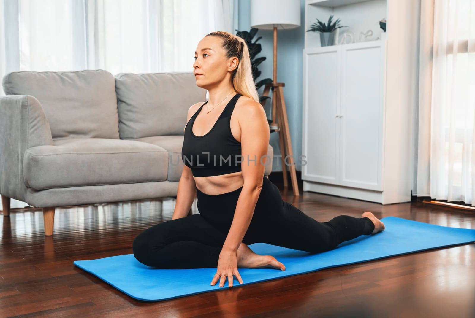 Senior woman in sportswear being doing yoga in meditation posture on exercising mat at home. Healthy senior pensioner lifestyle with peaceful mind and serenity. Clout