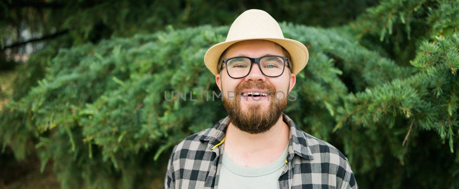 Laughing millennial man wearing hat over green tree background vertical - emotion and vacation travel holidays