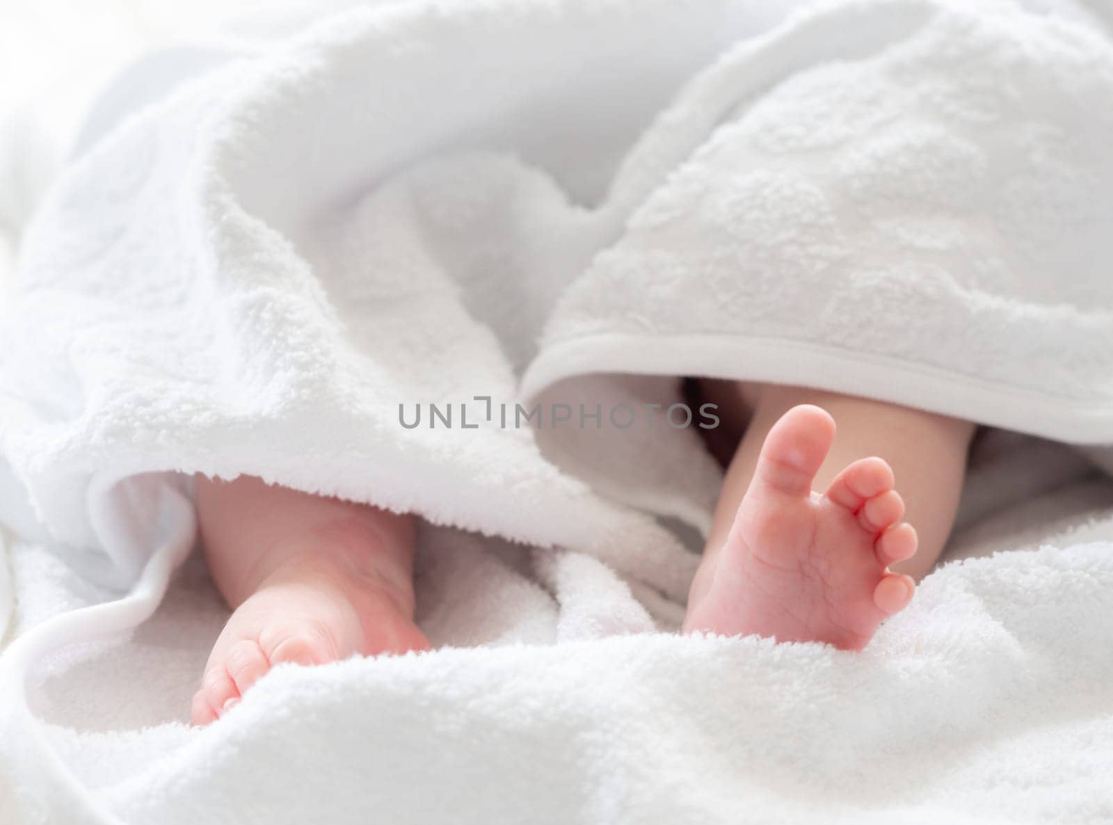 The tender feet and legs of a freshly bathed infant child peek from a plush white towel, capturing moments of innocence and warmth