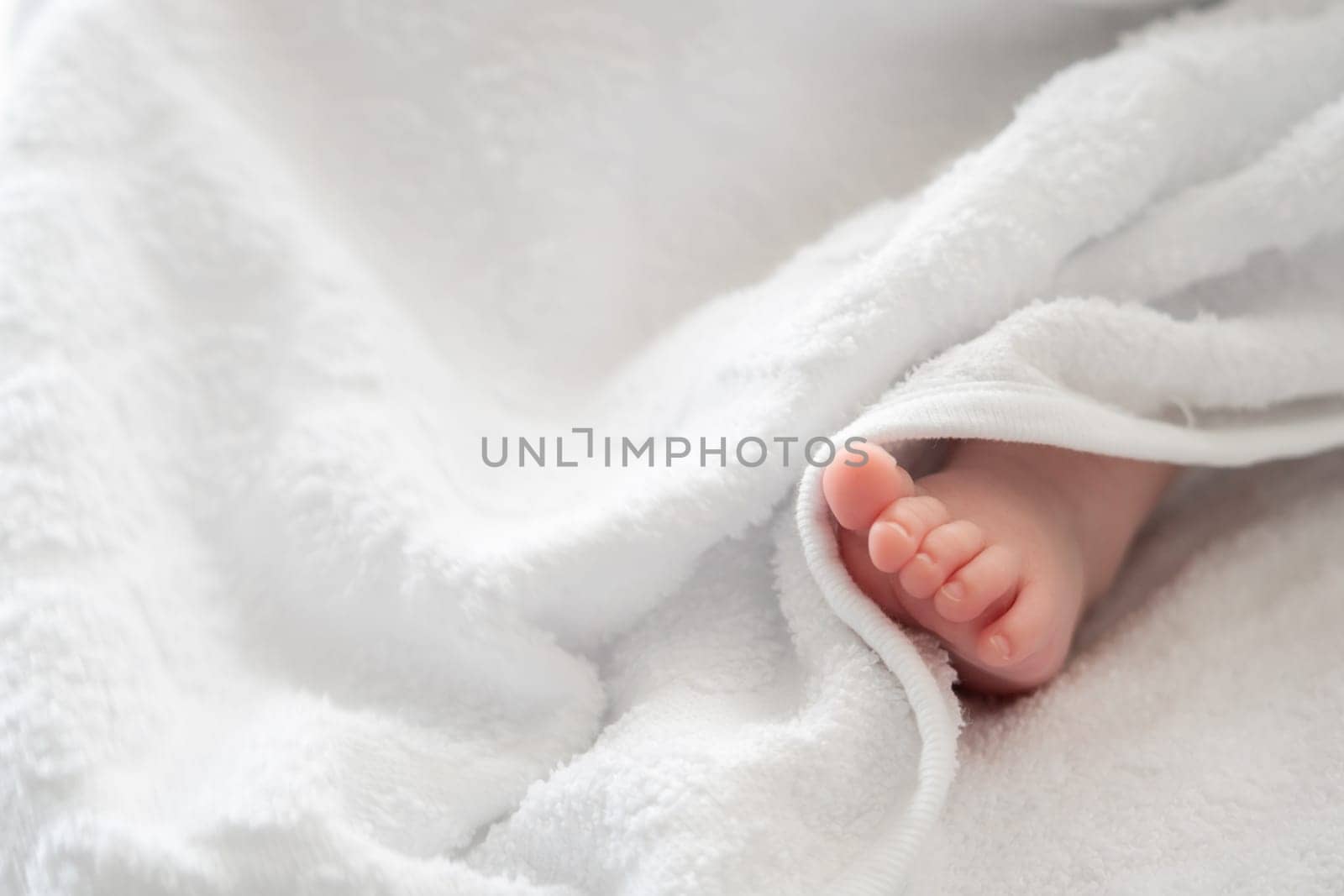 An endearing image showcasing the tiny foot of a baby, gracefully peeking out from the white embrace of a soft towel