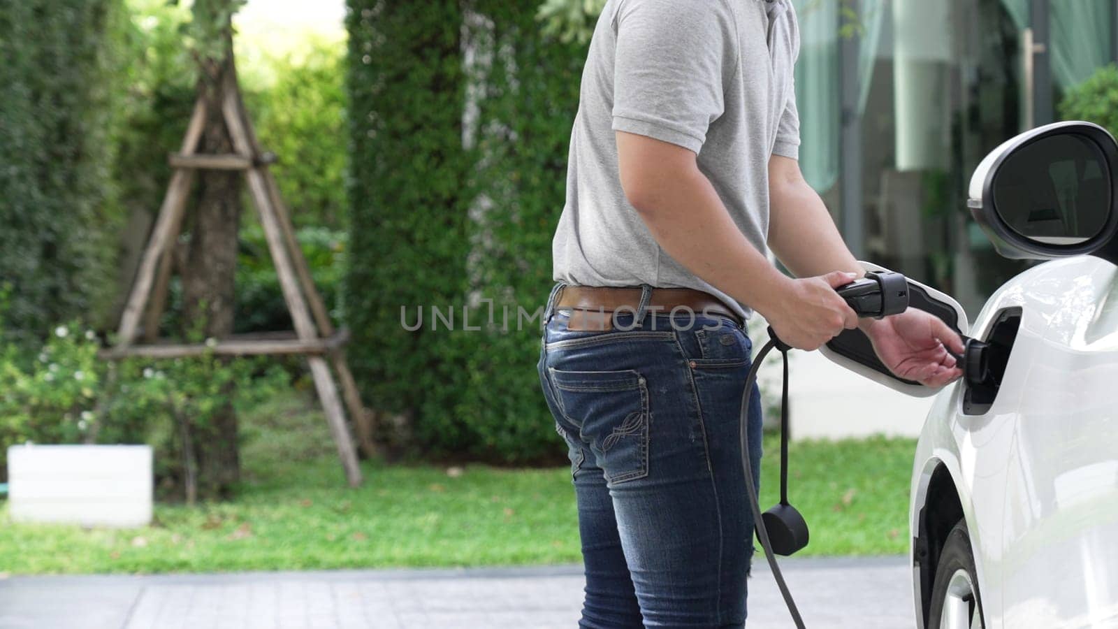 A man unplugs the electric vehicle's charger at his residence. Concept of the use of electric vehicles in a progressive lifestyle contributes to a clean and healthy environment.