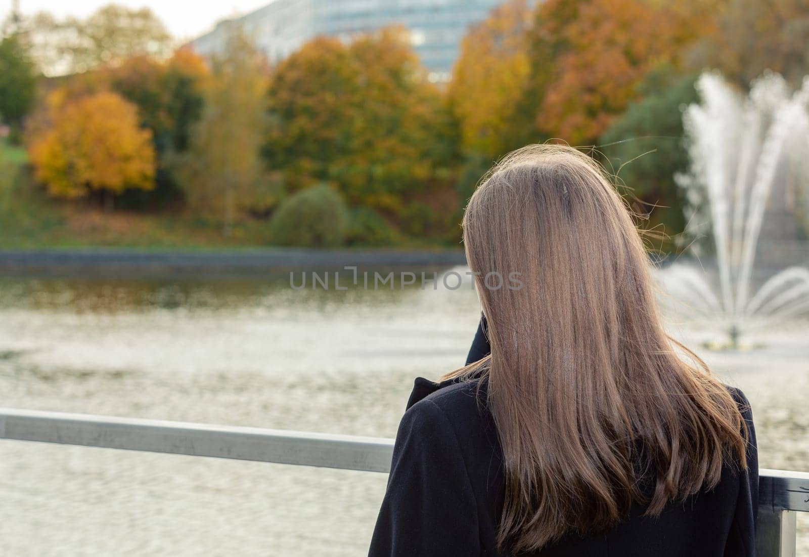 Portrait of a girl on a bridge near a pond in a city park against the backdrop of fountains